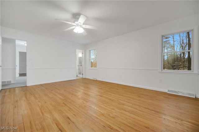 empty room with light wood finished floors, ceiling fan, visible vents, and baseboards