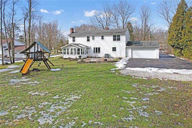 rear view of house featuring aphalt driveway, a playground, a garage, a sunroom, and a lawn