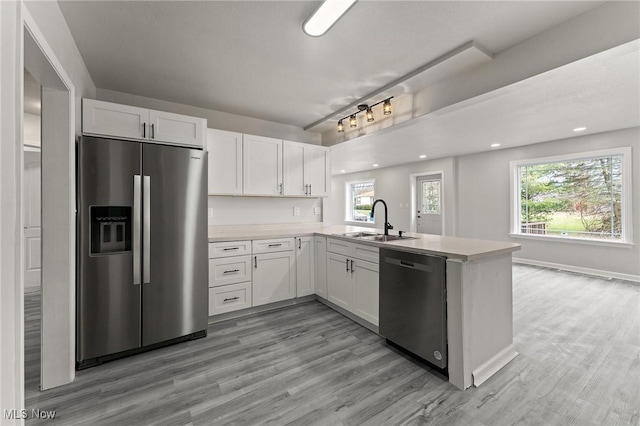 kitchen featuring appliances with stainless steel finishes, light countertops, a sink, and a peninsula