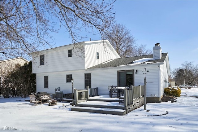 snow covered property with a fire pit, a chimney, and a wooden deck