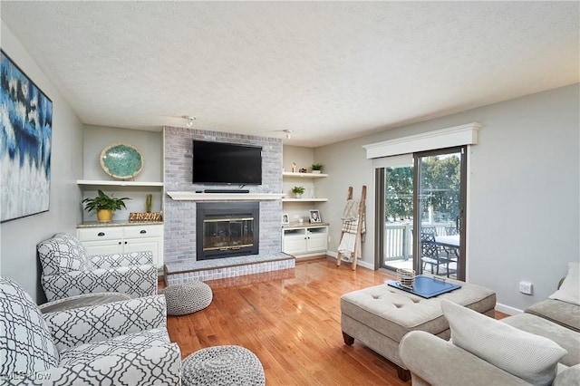 living room with light wood-style floors, a fireplace, baseboards, and a textured ceiling