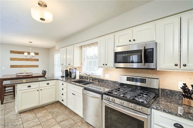 kitchen featuring decorative backsplash, a peninsula, stainless steel appliances, white cabinetry, and a sink