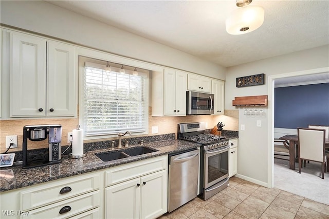 kitchen with decorative backsplash, dark stone countertops, stainless steel appliances, white cabinetry, and a sink