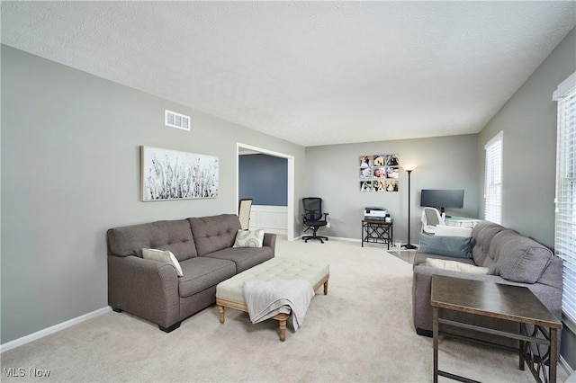 living area with light colored carpet, visible vents, a textured ceiling, and baseboards