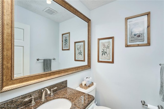 bathroom featuring a textured ceiling, toilet, vanity, and visible vents