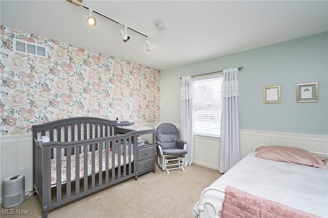 carpeted bedroom featuring rail lighting, a wainscoted wall, and visible vents