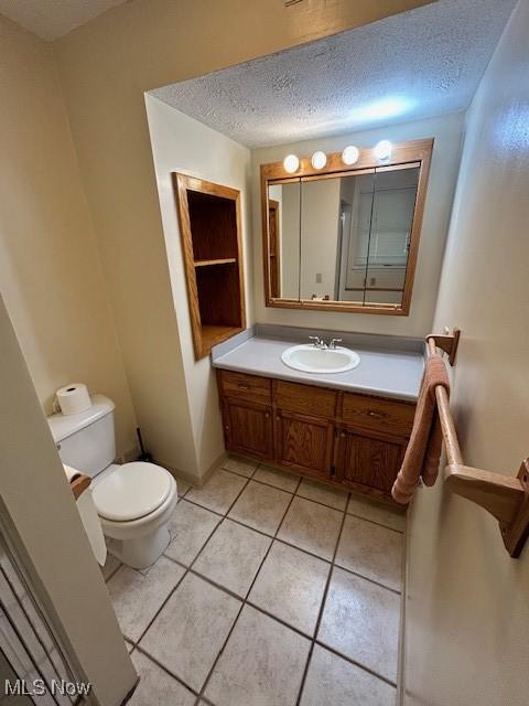 bathroom featuring a textured ceiling, toilet, vanity, baseboards, and tile patterned floors