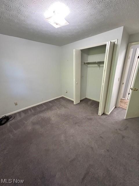 unfurnished bedroom with a closet, carpet flooring, a textured ceiling, and baseboards