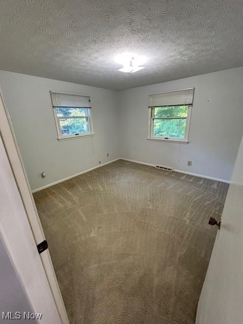 carpeted empty room with a textured ceiling, baseboards, visible vents, and a healthy amount of sunlight