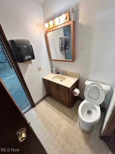 half bath with toilet, tile patterned floors, vanity, and baseboards