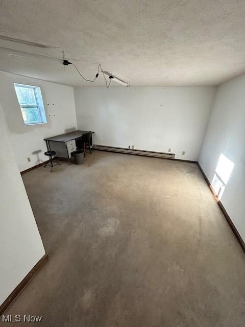 spare room featuring a baseboard heating unit, a textured ceiling, and baseboards