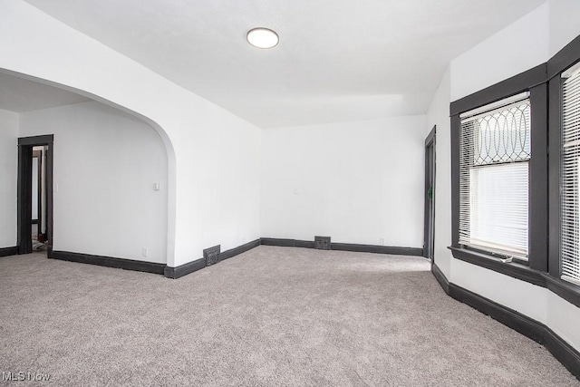 empty room featuring arched walkways, carpet flooring, and baseboards