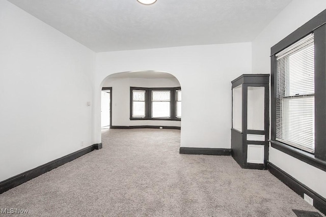 spare room featuring arched walkways, carpet floors, and baseboards