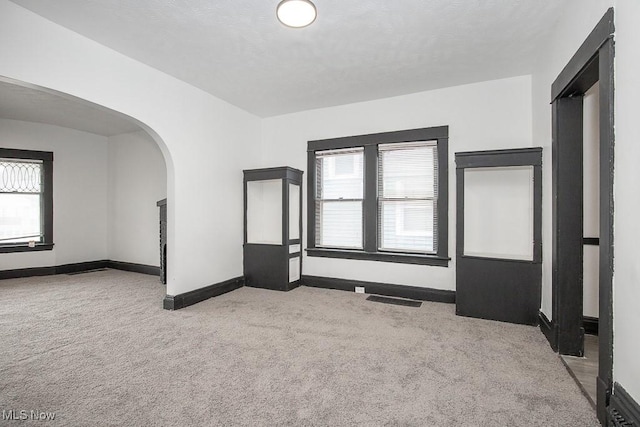 carpeted spare room with arched walkways, plenty of natural light, a textured ceiling, and baseboards