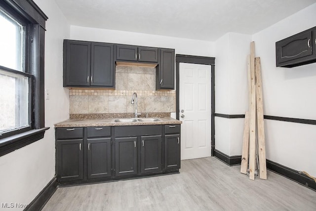 kitchen featuring light wood finished floors, baseboards, decorative backsplash, and a sink