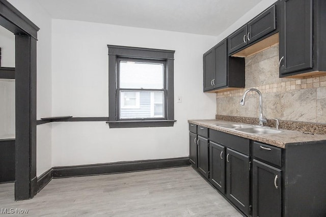 kitchen with light wood-style floors, baseboards, backsplash, and a sink