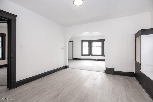 unfurnished room featuring baseboards, arched walkways, and wood finished floors