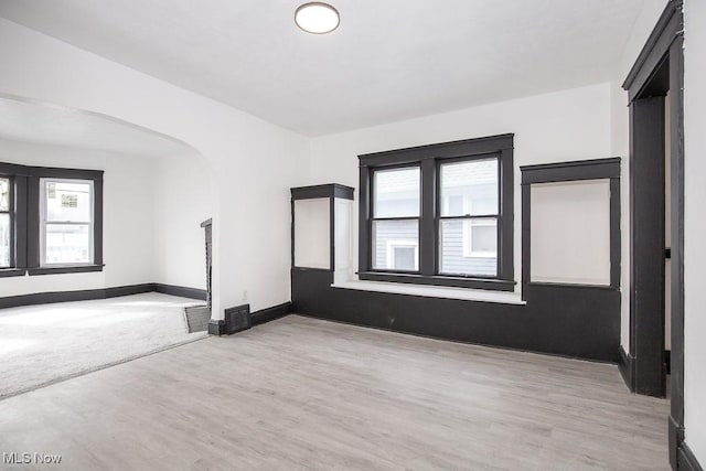 spare room featuring arched walkways, wood finished floors, and baseboards