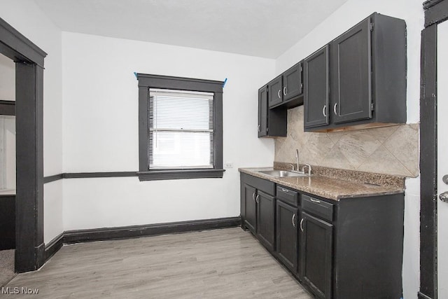 kitchen featuring baseboards, tasteful backsplash, a sink, and light wood-style floors