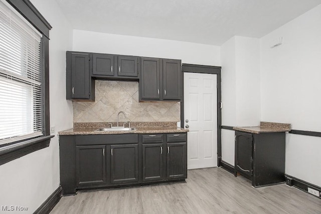 kitchen with baseboards, tasteful backsplash, a sink, and light wood-style floors