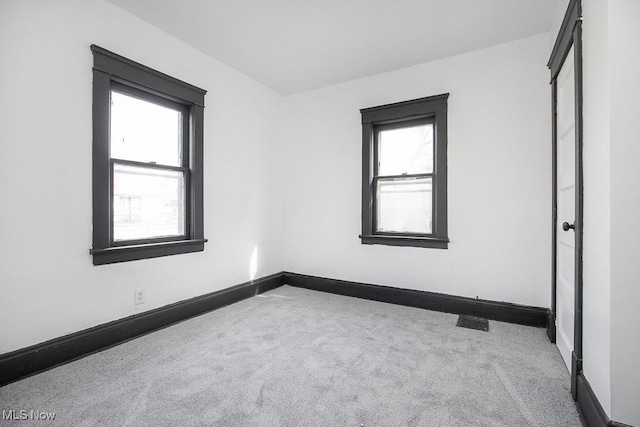 empty room featuring visible vents, carpet floors, a wealth of natural light, and baseboards