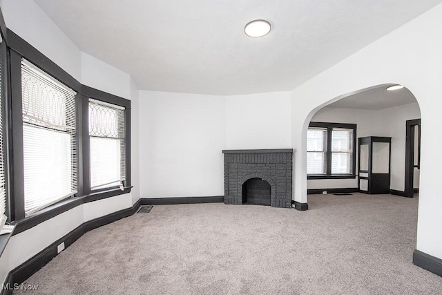 unfurnished living room featuring baseboards, arched walkways, visible vents, carpet, and a fireplace