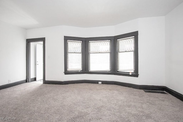 spare room featuring carpet floors, visible vents, baseboards, and a wealth of natural light