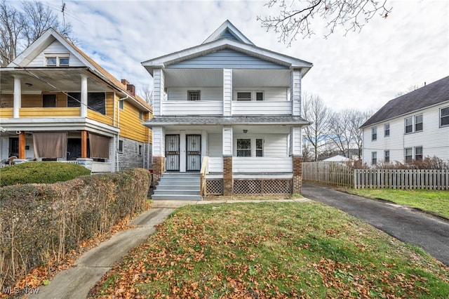 view of front facade featuring covered porch, fence, aphalt driveway, and a front yard