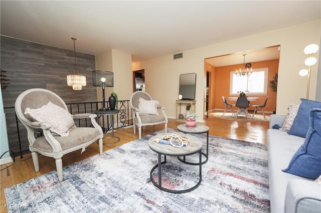 living room featuring an accent wall, wood finished floors, visible vents, and an inviting chandelier