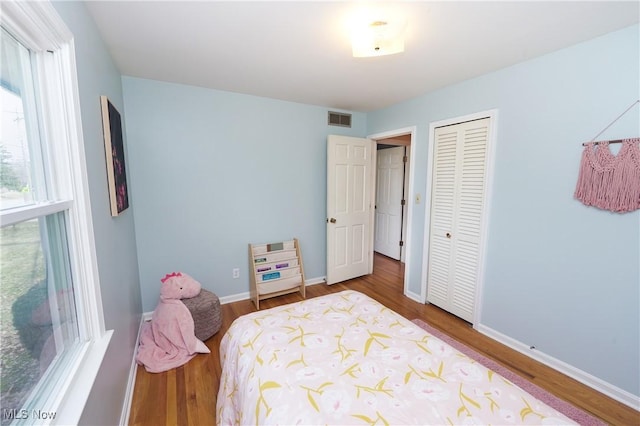 bedroom featuring a closet, visible vents, baseboards, and wood finished floors