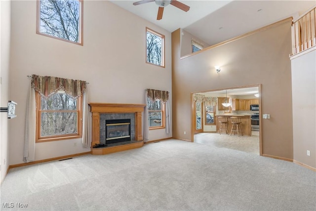 unfurnished living room featuring a fireplace, a high ceiling, a ceiling fan, carpet flooring, and baseboards