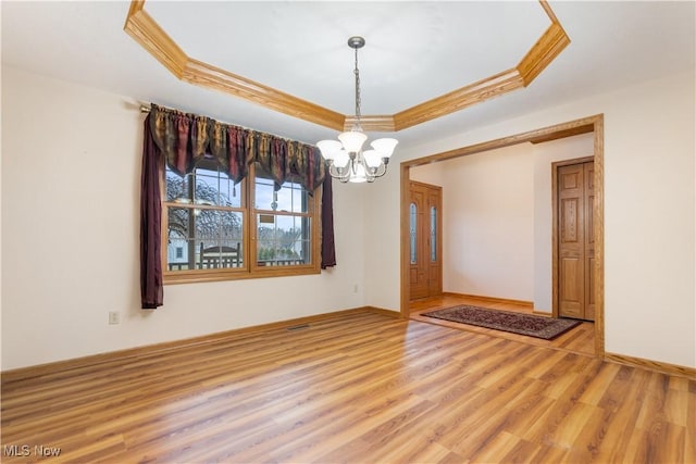 empty room with a tray ceiling, crown molding, a notable chandelier, wood finished floors, and baseboards