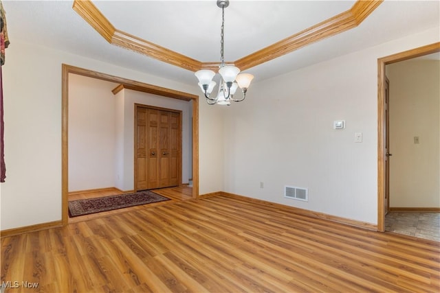 empty room featuring a chandelier, a tray ceiling, light wood-type flooring, and visible vents