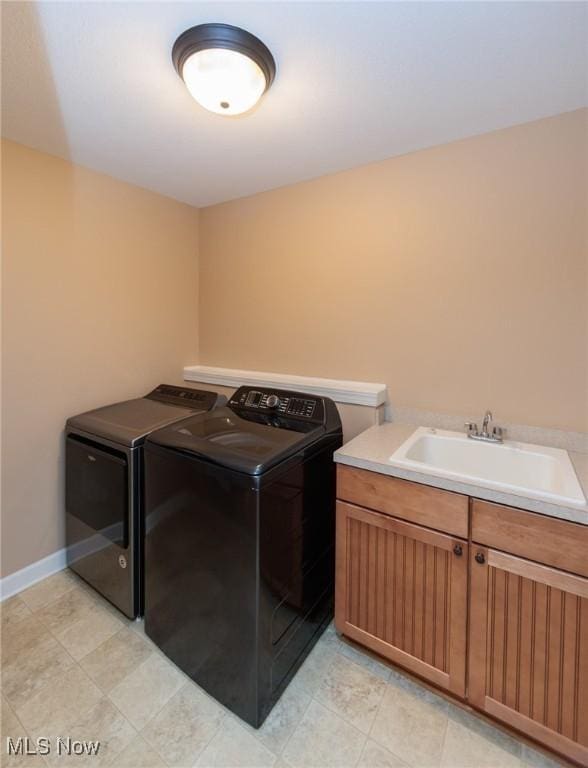 clothes washing area with washing machine and dryer, cabinet space, a sink, and baseboards