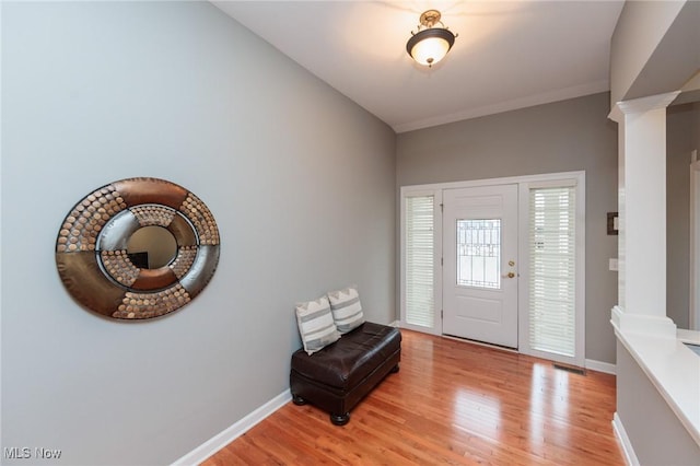 foyer entrance with light wood-style floors, baseboards, and ornate columns