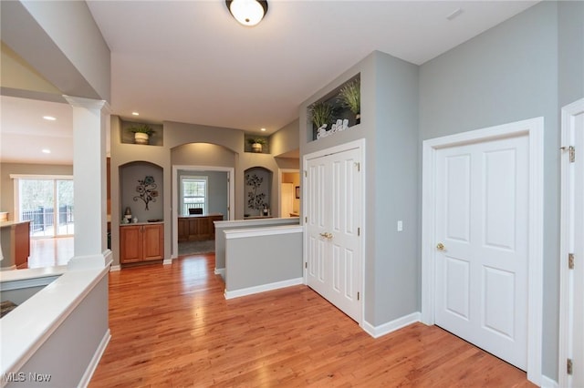 hallway featuring baseboards, recessed lighting, decorative columns, and light wood-style floors