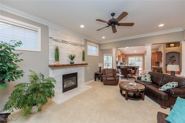 living area featuring light carpet, a fireplace, a ceiling fan, decorative columns, and crown molding