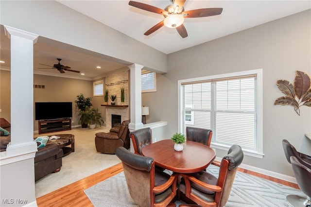 dining area with a large fireplace, light wood finished floors, visible vents, baseboards, and ornate columns