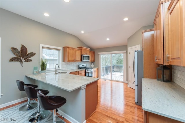 kitchen with light wood finished floors, stainless steel appliances, a sink, a peninsula, and a kitchen breakfast bar