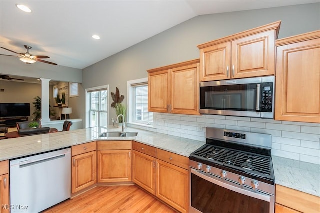 kitchen with appliances with stainless steel finishes, a sink, decorative backsplash, and light stone counters