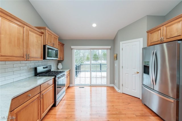 kitchen with decorative backsplash, lofted ceiling, light stone countertops, stainless steel appliances, and light wood-style floors