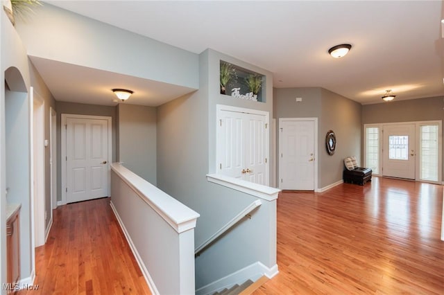 hall featuring light wood-style floors, baseboards, and an upstairs landing