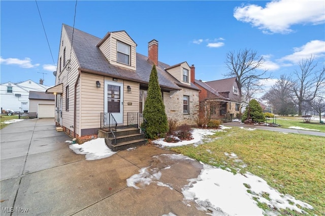 new england style home with a detached garage, an outdoor structure, a chimney, and a front lawn