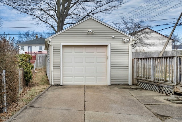 detached garage featuring concrete driveway and fence