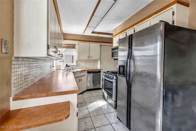 kitchen with light tile patterned floors, stainless steel appliances, light countertops, backsplash, and a sink