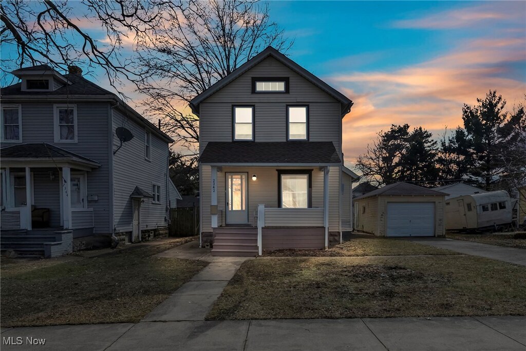 traditional-style home featuring driveway, a garage, an outbuilding, a porch, and a front yard