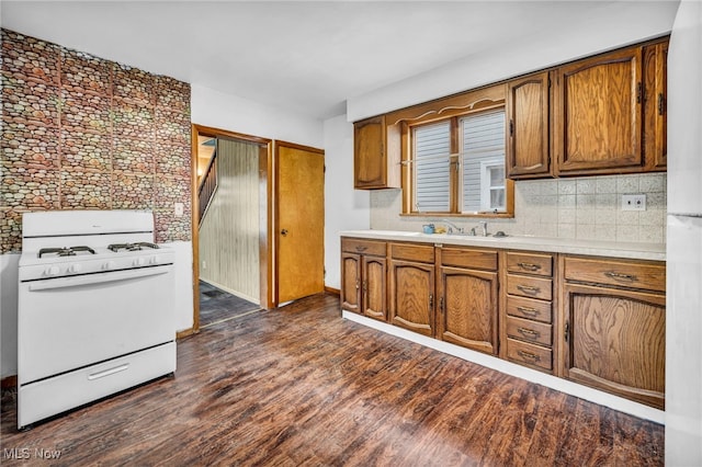 kitchen featuring white gas range oven, brown cabinetry, dark wood finished floors, light countertops, and a sink