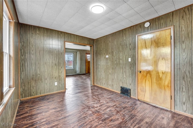 unfurnished room featuring visible vents, wooden walls, baseboards, and wood finished floors