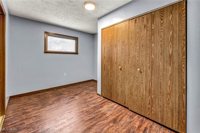 unfurnished bedroom with a textured ceiling, a closet, wood finished floors, and baseboards