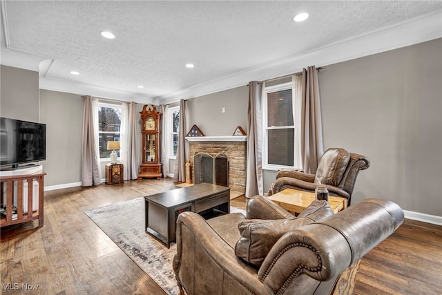 living area with a stone fireplace, a textured ceiling, baseboards, and wood finished floors